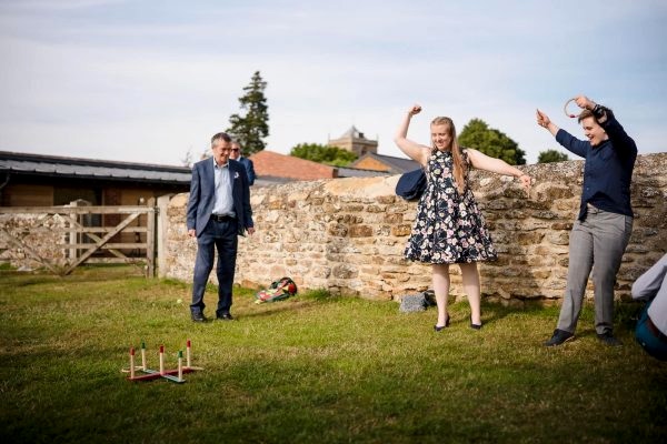 Dodford Manor Wedding Photographer captures a group of people playing a game of croquet in a field.