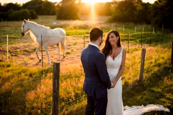A bride and groom standing in front of a horse in a field at sunset, captured beautifully by a Dodford Manor Wedding Photographer.