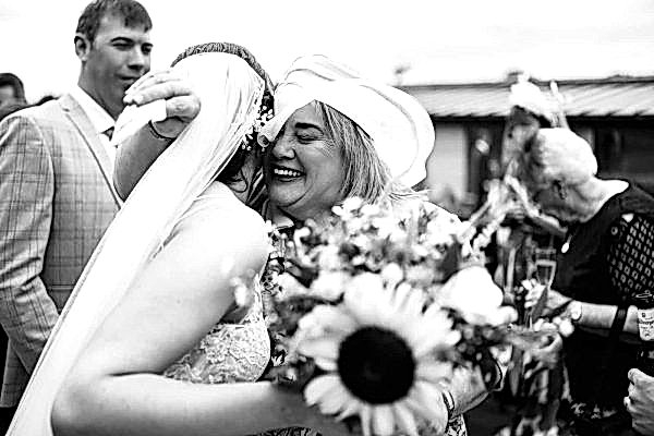 At a Dodford Manor wedding, a bride tightly embraces her bridesmaid in an emotional moment captured by the photographer.