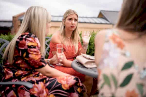 Dodford Manor Wedding Photographer capturing three women sitting at an outdoor table engaged in lively conversation.
