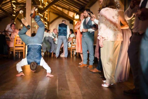 A man, captured by the keen eye of a Dodford Manor Wedding Photographer, gracefully performs a handstand on the dance floor during a joyous wedding reception.