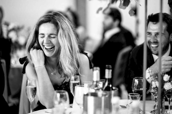 Dodford Manor Wedding Photographer: Black and white photo of a woman laughing at a table.