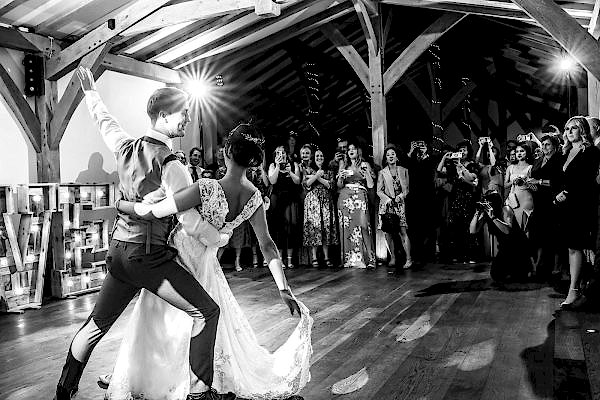 Dodford Manor Wedding Photographer captures a memorable moment of a bride and groom as they elegantly share their first dance in a rustic barn setting.