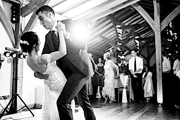 Dodford Manor Wedding Photographer captures the magical moment of a bride and groom sharing their first dance in a rustic barn setting.