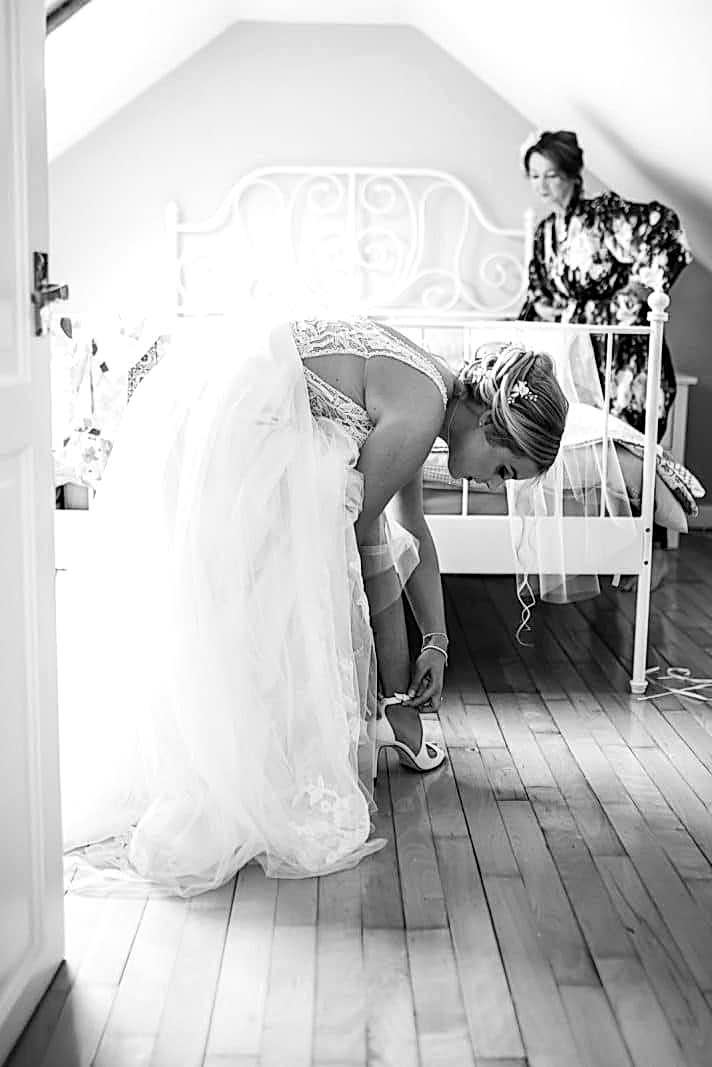 A bride at Dodford Manor putting on her wedding shoes in a bedroom.