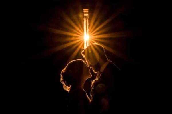 A Dodford Manor Wedding Photographer captures a bride and groom as they are silhouetted against a light bulb.