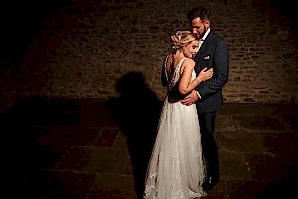Dodford Manor Wedding Photographer: Capturing an intimate moment amidst dimly-lit surroundings, this image portrays a tender embrace between a bride and groom.