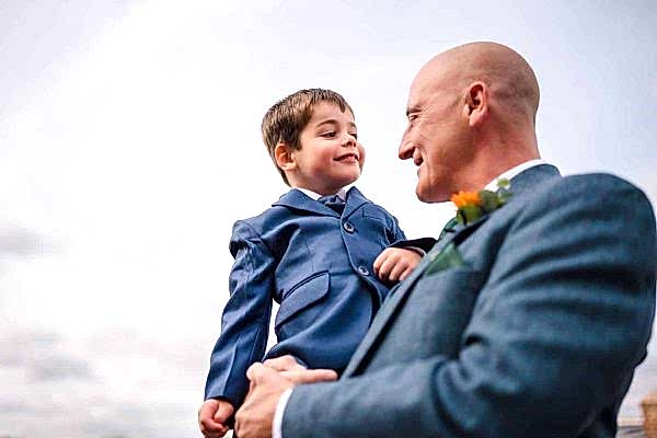 A man in a suit holding a young boy, captured by the Dodford Manor Wedding Photographer.
