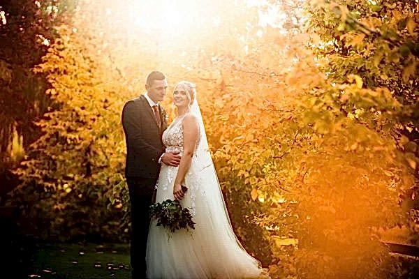 A bride and groom posing in front of autumn trees captured by Dodford Manor Wedding Photographer.