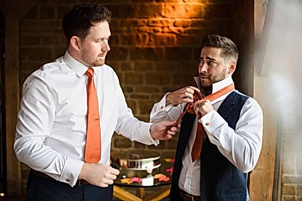 Dodford Manor Wedding Photographer capturing two men adjusting their ties in a room.
