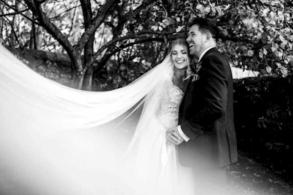 Dodford Manor Wedding Photographer: A stunning black and white photo capturing the tender moment of a bride and groom in front of a majestic tree.
