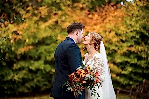 A Dodford Manor Wedding Photographer captures a blissful bride and groom kissing amidst vibrant autumn leaves.