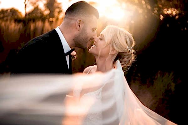 A Dodford Manor Wedding Photographer captures a romantic moment as the bride and groom share a kiss in front of a breathtaking sunset.