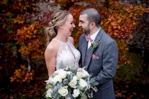 Dodford Manor Wedding Photographer captures the joyful moments of a bride and groom as they smile in front of autumn leaves.
