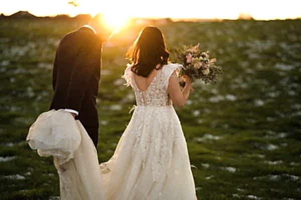 A bride and groom captured by a Dodford Manor Wedding Photographer while walking through a field at sunset.