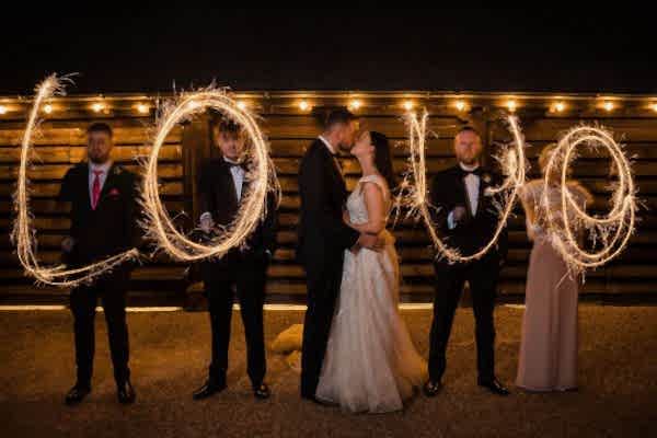 A group of bridesmaids and groomsmen at Dodford Manor Wedding Photographer are holding sparklers and writing 'love'.