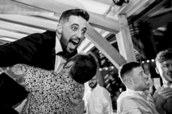 A Dodford Manor wedding photographer captures the heartfelt moment of one man embracing another man on the dance floor.