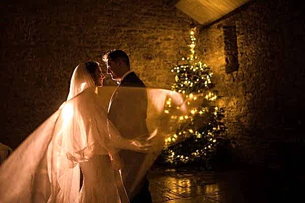 A bride and groom captured beautifully in front of a Christmas tree by a skilled Dodford Manor Wedding Photographer.