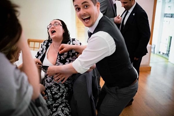 People laughing and unzipping a woman's dress at party.