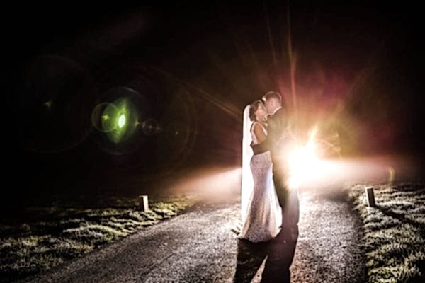 A bride and groom, captured by a Dodford Manor Wedding Photographer, standing on a road at night.