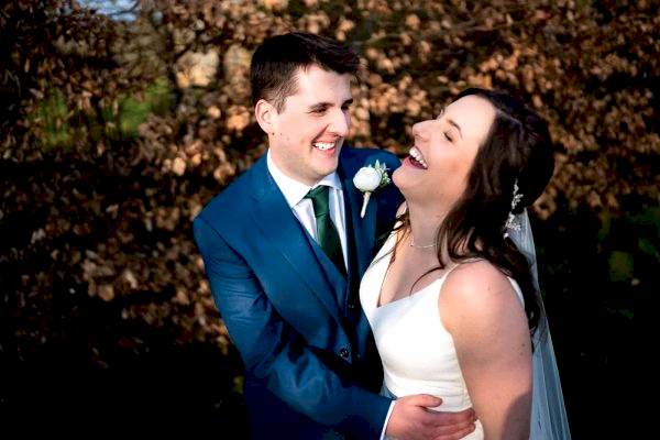 Dodford Manor Wedding Photographer captures a bride and groom laughing in front of a tree.