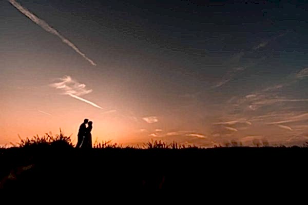 A Dodford Manor Wedding Photographer capturing a silhouette of a couple standing in a field at sunset.