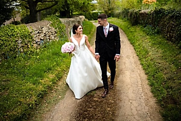 A Dodford Manor wedding photographer capturing a bride and groom walking down a dirt road.