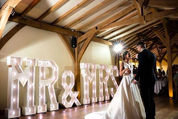 A Dodford Manor Wedding Photographer captures the special moment of a bride and groom standing in front of Mr and Mrs letters.