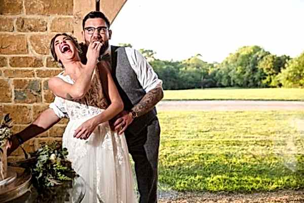 A bride and groom laughing while cutting their wedding cake captured by a Dodford Manor Wedding Photographer.