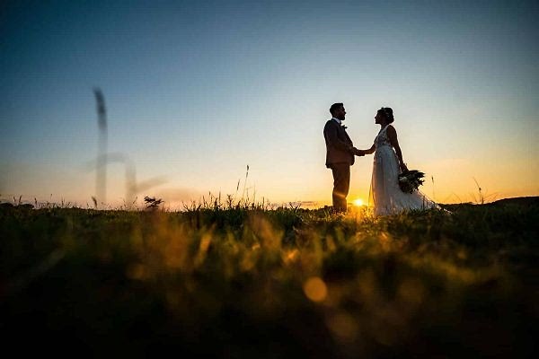 Dodford Manor Wedding Photographer capturing a mesmerizing bride and groom standing in a radiant field at romantic sunset.