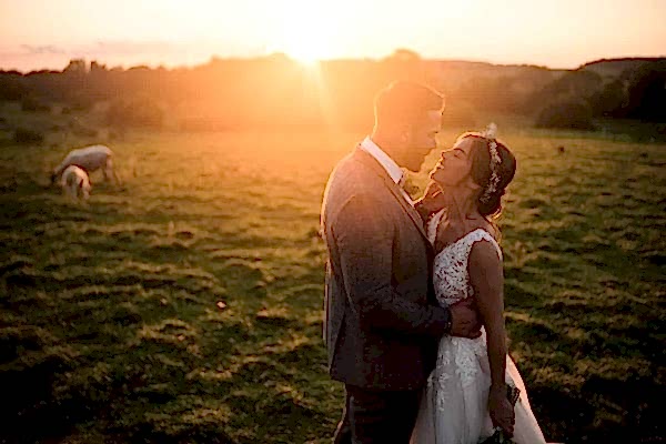 Dodford Manor Wedding Photographer captures a stunning sunset moment with the bride and groom standing in a field.