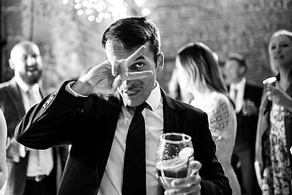 A black and white photo of a man making a face with a glass of beer, captured by the Dodford Manor Wedding Photographer.