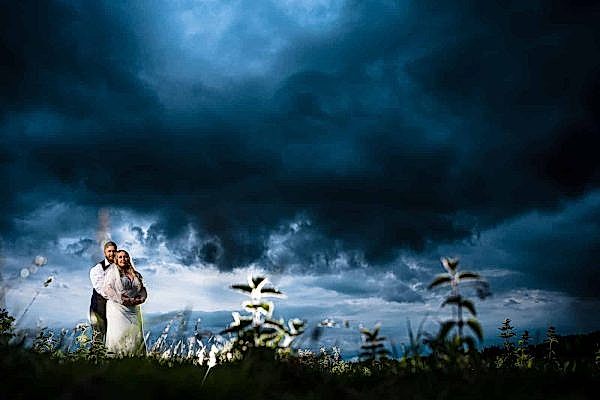 A Dodford Manor wedding photographer capturing a bride and groom standing under a stormy sky.