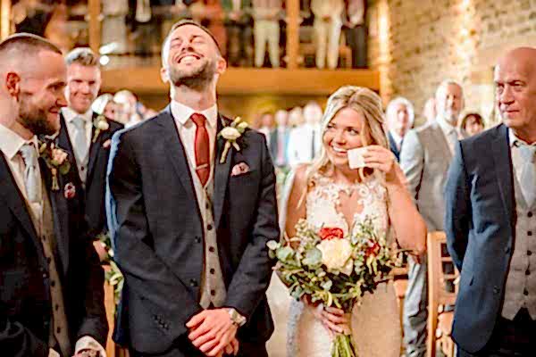 A Dodford Manor wedding photographer captures the joyful moments as the bride and groom laugh at each other during their ceremony.