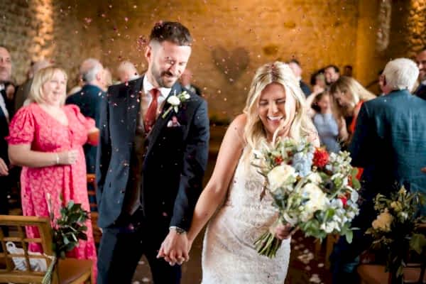 A bride and groom beautifully walk down the aisle at Dodford Manor with confetti joyfully thrown at them.