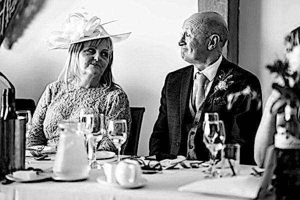 A man and woman sitting at a table with hats on, captured by the Dodford Manor Wedding Photographer.