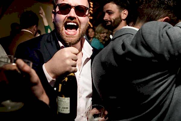 A man holding a bottle of wine at a party, captured beautifully by Dodford Manor Wedding Photographer.