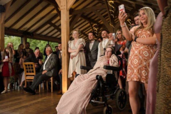 A Dodford Manor wedding photographer captures a woman in a wheelchair taking a picture of the crowd.