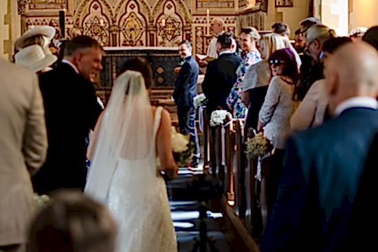 A bride walks down the aisle toward a groom in a church, while guests stand on either side, capturing every cherished moment. With the benefits of two wedding photographers, each angle of this beautiful journey is beautifully preserved forever.
